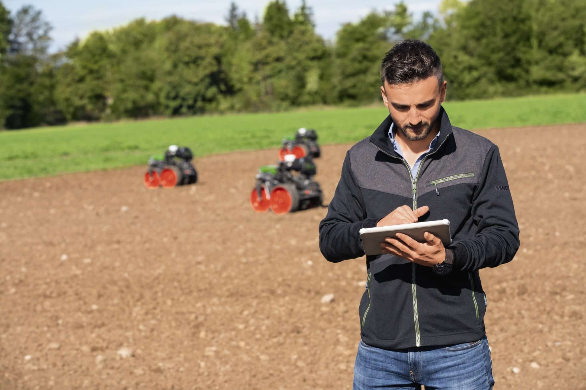 Mann am Feld mit Robotern im Hintergrund.